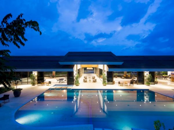 A luxurious pool area with a modern building illuminated at night; the sky is blue with scattered clouds.