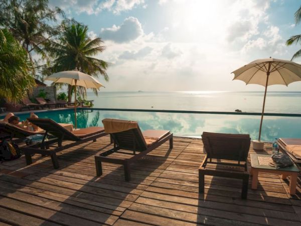 A serene poolside with lounge chairs, umbrellas, and a scenic view of the ocean under a cloudy sky.