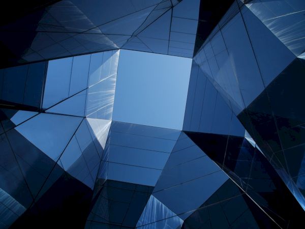 The image shows a geometric architectural structure with reflective glass surfaces and a view of the sky at the center.