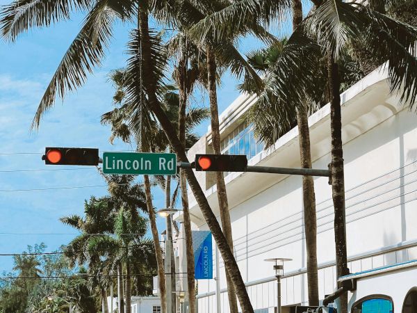 A street scene with palm trees, cars, and a sign for Lincoln Rd. Traffic lights and buildings are also visible.
