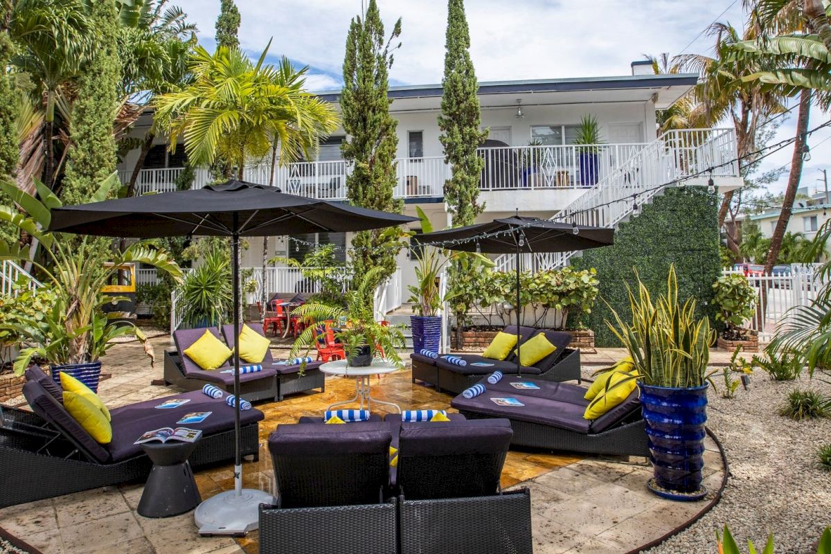 A poolside seating area with black lounge chairs, yellow pillows, and black umbrellas.