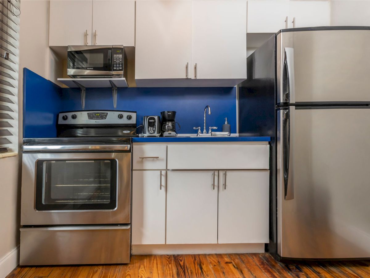 A modern kitchen with stainless steel appliances, including a fridge and stove, blue backsplash, and white cabinets.