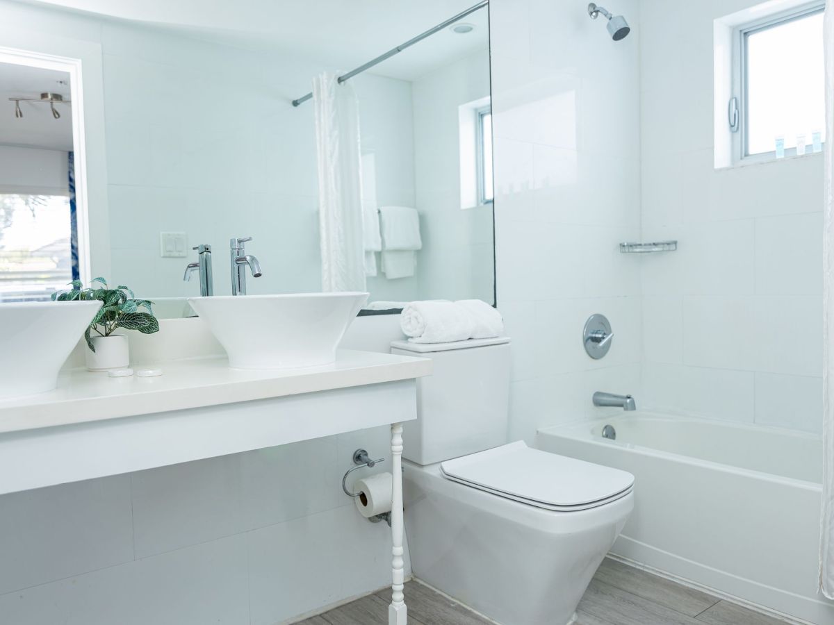 The image shows a modern bathroom with a sink, toilet, bathtub, and mirrors in a minimalist, bright design.