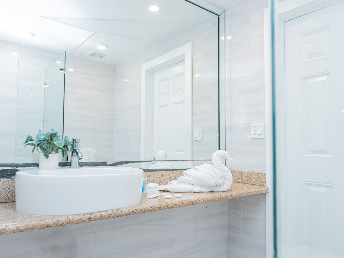 A modern bathroom with a large mirror, countertop sink, potted plant, and a towel folded into a swan on the counter.