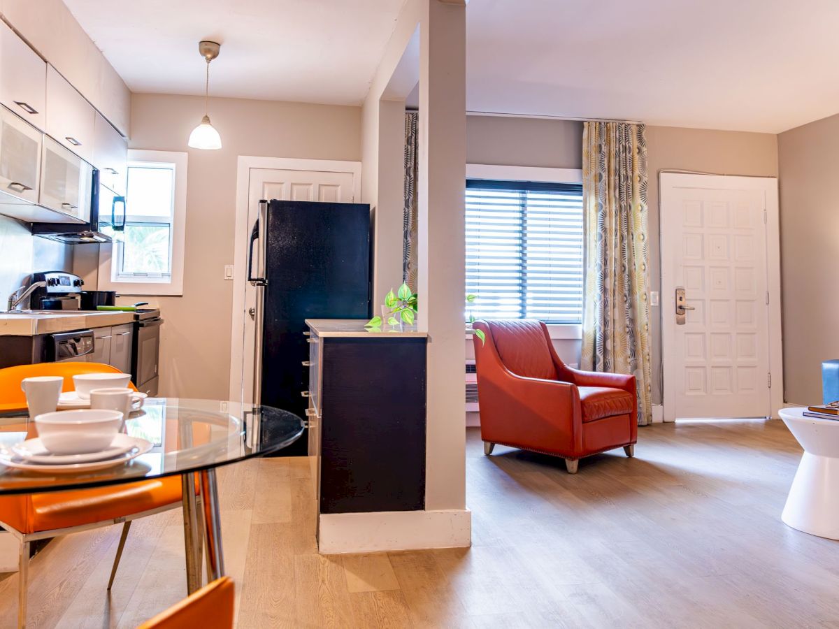 The image shows a modern open-plan kitchen and living area with a glass dining table, orange chairs, and cozy seating with ambient lighting.