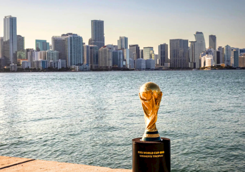 World&rsquo;s largest trophy on a pier by a sparkling harbor with a city skyline in the background, shimmering water, and a clear sky.