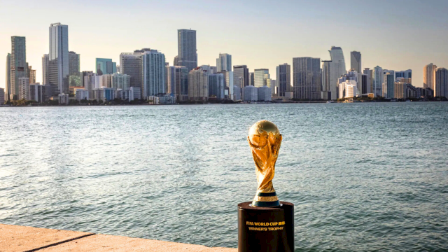 World&rsquo;s largest trophy on a pier by a sparkling harbor with a city skyline in the background, shimmering water, and a clear sky.